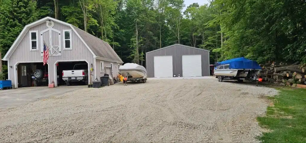 Gray steel workshop with two roll-up doors beside gambrel garage.