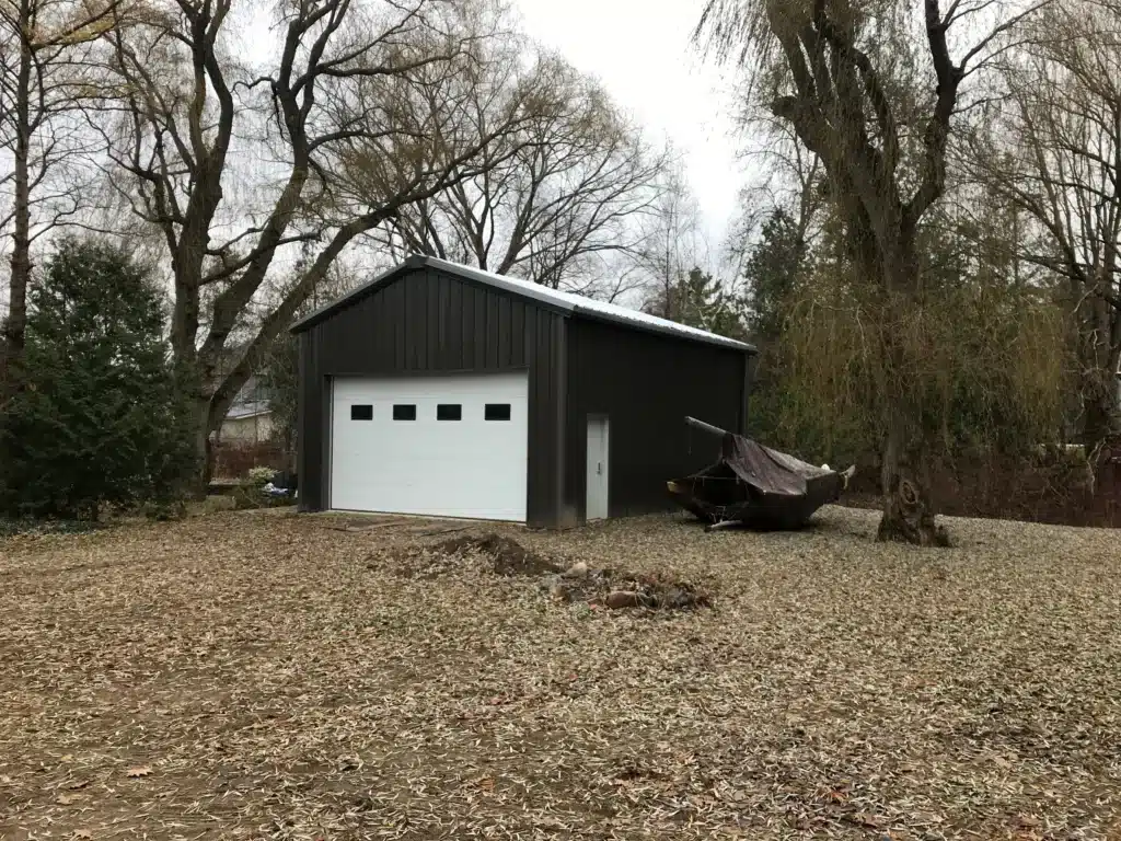 Dark steel garage with white roll-up door outdoors.